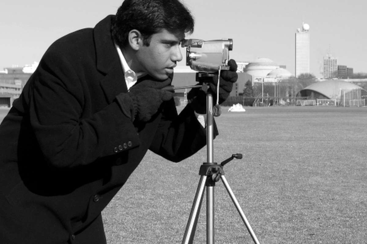 A photographer using a camera outdoors in a classic black-and-white scene.