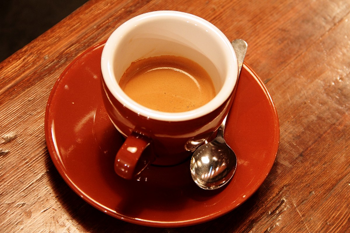 A cup of coffee beside roasted coffee beans on a light surface.
